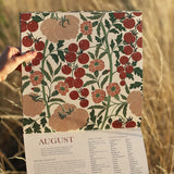 Hand holding a calendar with a floral and fruit pattern against a natural background