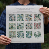 Person holding a gardening calendar with vegetable, fruit, and flower illustrations.