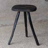 Black wooden stool with a rustic finish on a concrete floor.