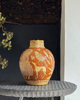 Decorative vase with intricate designs on a small table against a dark wall.