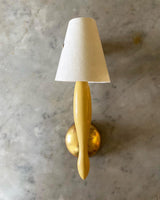 A wall-mounted light fixture with a beige stem and a white, conical lampshade, with a gold wall base.