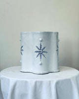 Decorative white container with blue floral design on a white tablecloth against a light gray background