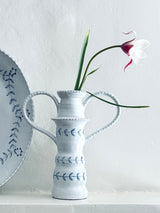 White ceramic pitcher with floral design holding a single flower against a light gray background