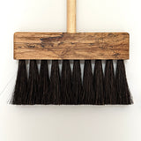 Wooden push broom with black bristles on a white background