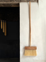 Wooden broom leaning against a white wall next to a dark fireplace.