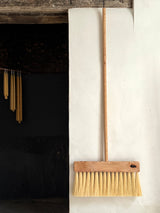 Wooden broom leaning against a white wall next to a dark fireplace.
