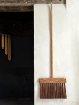 Wooden broom leaning against a white wall next to a dark fireplace.