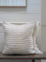 A hand-stitched white cushion made of wool, mohair, and boucle wool, displayed on a wooden surface against a white background.