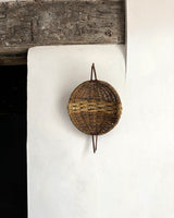Woven basket hanging on a white wall with a wooden shelf above