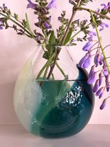 Teal and white glass vase with purple flowers on a light pink background