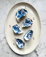 Five blue and white porcelain oyster shell dishes numbered 1 through 5 on an oval cream-colored serving platter, set on a white and gray marble surface.