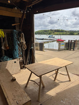 Wooden table on a dock with boats and greenery in the background