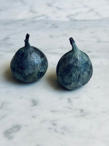 Two solid bronze figs with verdigris finish resting on a white marble surface.