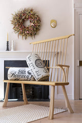 Wooden armchair with decorative pillows in a room with a wreath on the wall.