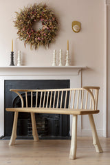 A wooden settle bench with a low back, made of oak and ash, positioned in a room with a fireplace and decorative items.