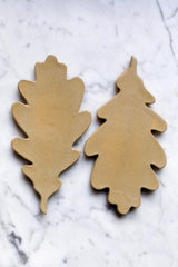 A set of beige ceramic Oak Leaf shaped trivets arranged on a marble surface.