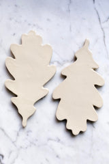 A set of beige ceramic Oak Leaf shaped trivets arranged on a marble surface.