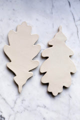 A set of beige ceramic Oak Leaf shaped trivets arranged on a marble surface.