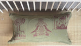 A cushion with a hand-block-printed design featuring illustrations of people and nature, in a green color, displayed on a shelf with other decorative items.