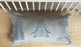 A cushion with a hand-block-printed design featuring illustrations of people and nature, in a green color, displayed on a shelf with other decorative items.