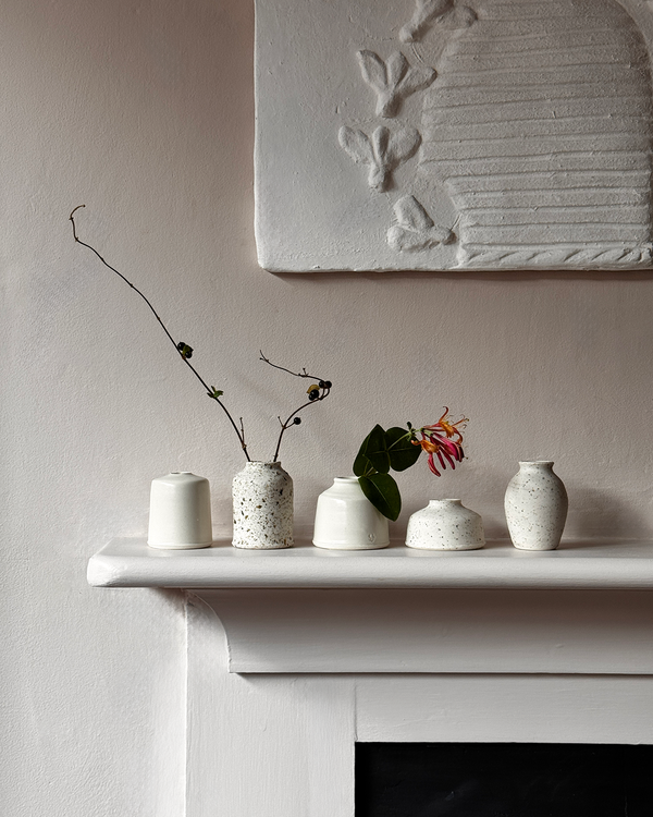 Set of small ceramic vases on a mantelpiece with a decorative wall piece in the background.