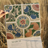 Decorative calendar with floral and fruit patterns held against a natural background