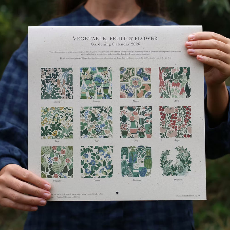 Person holding a gardening calendar with vegetable, fruit, and flower illustrations.