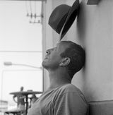 Man leaning against a wall with a hat on his head, black and white photo