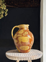 Decorative ceramic pitcher with cow design on a small round table against a dark background