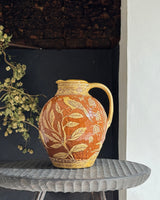 Decorative ceramic pitcher with bird and leaf patterns on a small table.