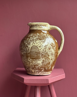 Decorative ceramic pitcher with floral and honeycomb design on a pink stand against a pink wall.