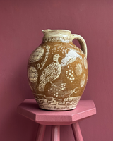 Ceramic pitcher with bird design on a pink stool against a pink wall