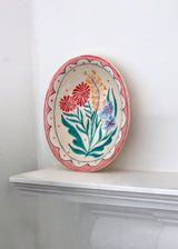Decorative plate with floral design on a white shelf against a white wall
