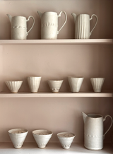 Collection of ceramic pots and jugs on shelves against a neutral background