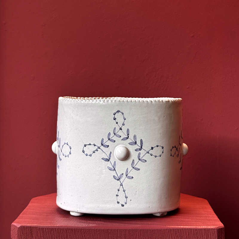 White ceramic planter with floral patterns on a red surface against a red wall