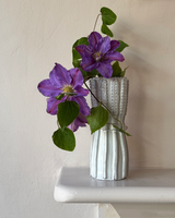 Silver textured vase with purple flowers on a white surface against a beige wall