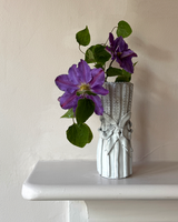 Silver vase with purple flowers on a white surface against a beige wall
