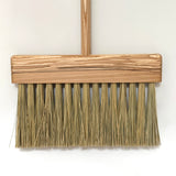 Wooden push broom with straw bristles on a white background