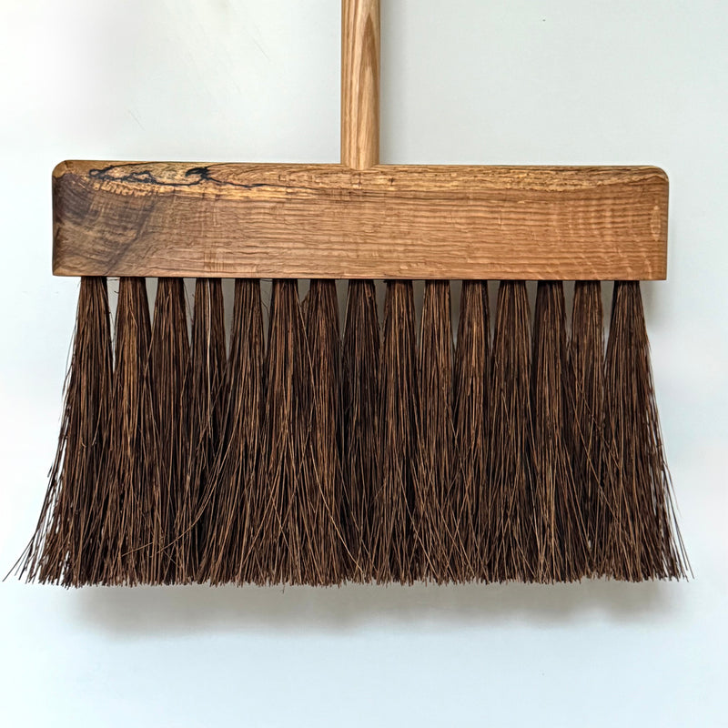 Wooden broom with brown bristles on a white background