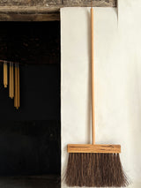 Wooden broom leaning against a white wall next to a dark fireplace.