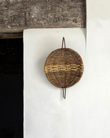 Woven basket hanging on a white wall with a wooden shelf above