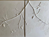 Two square white ceramic wall tiles featuring embossed oak leaves and acorns in a raised relief design, shown side-by-side against a neutral background.