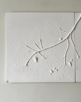 White textured wall art featuring embossed botanical branches and leaves, mounted on a light neutral wall.