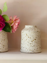 Two speckled ceramic vases with flowers on a neutral background
