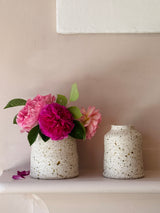 Two speckled ceramic vases with pink flowers on a neutral background