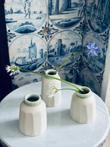 Three small white vases with flowers against a decorative blue and white tile wall.