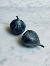 Two solid bronze verdigris figs resting on a white marble surface.